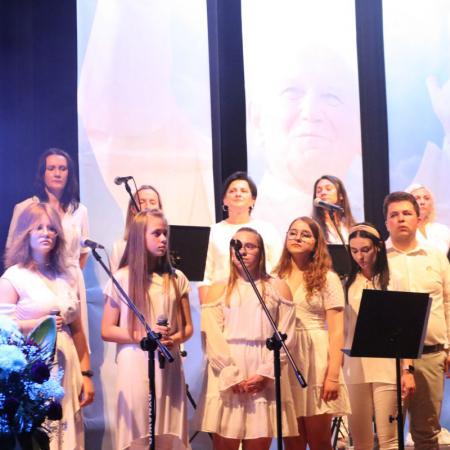 Grupa osób śpiewa a scenie podczas Koncertu Uwielbienia