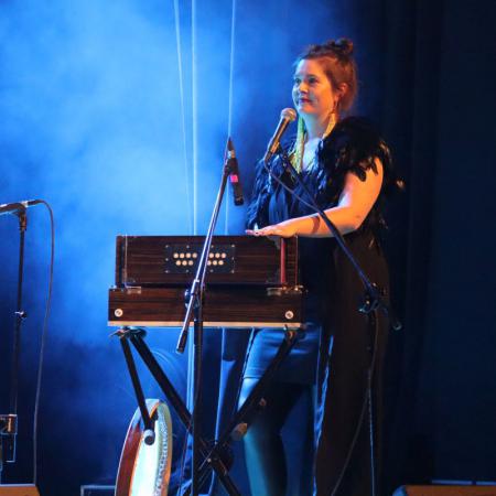 Kobieta z zespołu "KOSY" śpiewa i  gra na instrumencie podczas koncertu