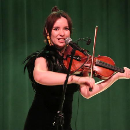 Kobieta z zespołu "KOSY' śpiewa i gra na skrzypcach na scenie