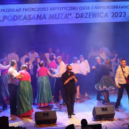 Grupa osób śpiewa i tańczy na scenie