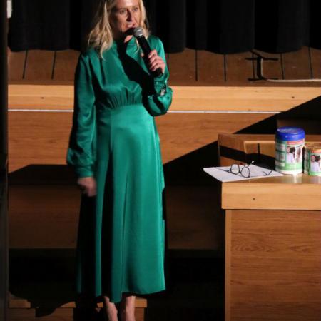 Kobieta w zielonej sukience przemawia przy mikrofonie przed sceną 