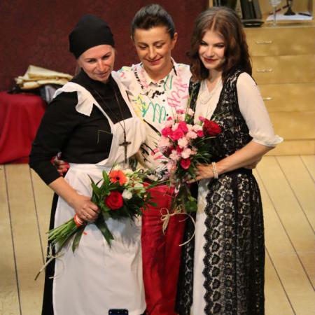 Trzy kobiety stoją na scenie i trzymają kwiaty  