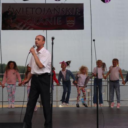 Uczestnik WTZ śpiewa przy mikrofonie, z tyłu tańczą przedszkolaki