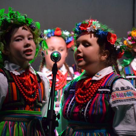 Dziewczynki w ludowych strojach śpiewają przy mikrofonie na scenie