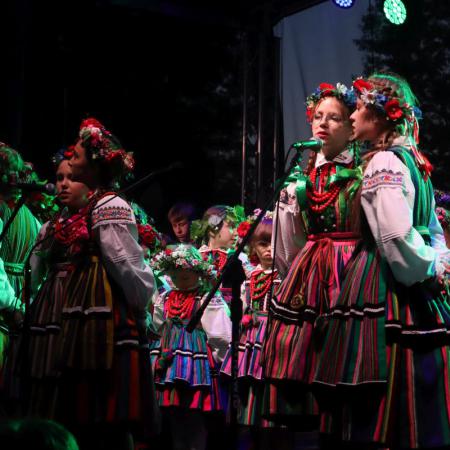 Dzieci w strojach ludowych śpiewają przy mikrofonie na scenie