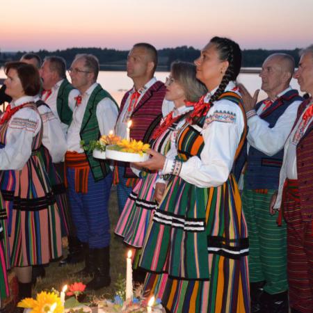 Grupa osób w ludowych strojach niesie wianki do wody