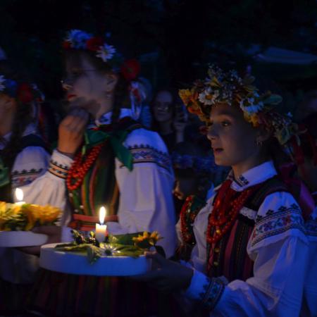 Dziewczyny w strojach ludowych niosą wianki do wody