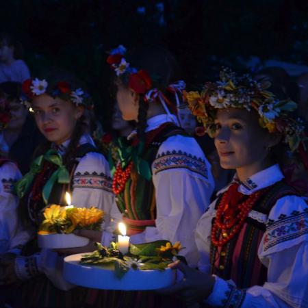 Dziewczyny w strojach ludowych niosą zapalone wianki do wody