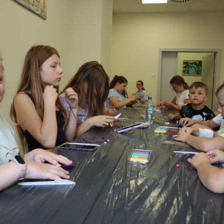 Grupa dzieci siedzi przy stole nakrytym czarną folią i wykonuje prace plastyczną z plasteliny.