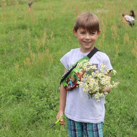 Chłopiec stoi na łące i trzyma w ręku kwiaty