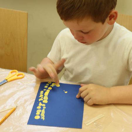 Chłopiec maluje farbami prace plastyczną