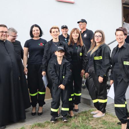 Grupa osób w strażackich strojach wraz z księżmi stoją przed budynkiem świetlicy w Domasznie.