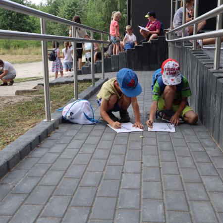 Chłopcy kucają na chodniku i szkicują obrazy węglem