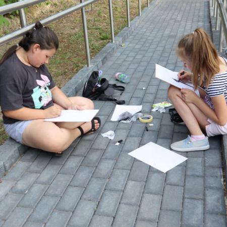 Dziewczyny siedzą na chodniku i szkicują swoje obrazy 