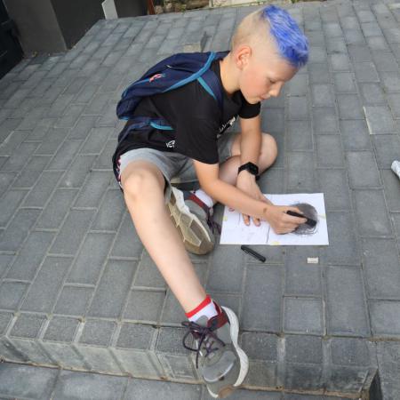 Chłopiec siedzi na chodniku i szkicuje obraz węglem