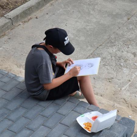 Chłopiec siedzi na chodniku i maluje obraz