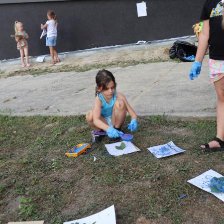 Dziewczynka siedzi na trawniku i maluje farbami 
