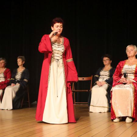 Kobieta w czerwonej sukience recytuje wiersz o dziejach Drzewicy na scenie