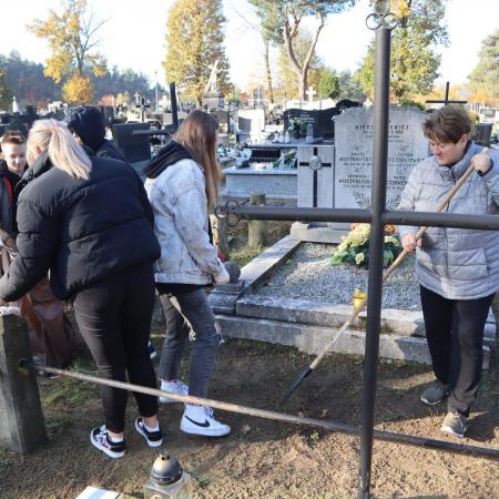 Kobieta z TPD wraz z młodzieżą sprzątający zabytkowy grób na cmentarzu w Drzewicy
