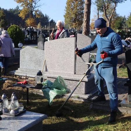 Mężczyzna kosi trawę przy zabytkowych pomnikach na cmentarzu