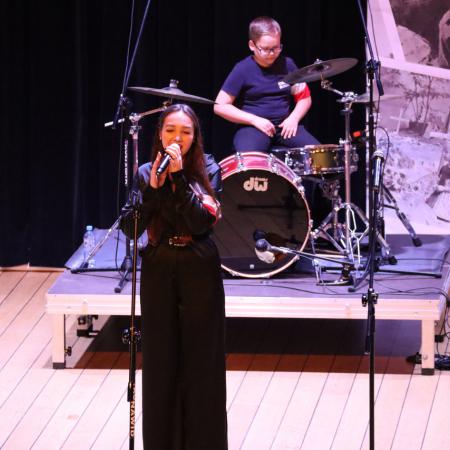 Dziewczyna w czarnym stroju śpiewa przy mikrofonie na scenie