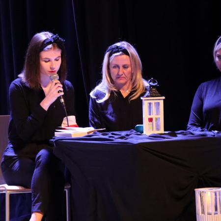 Trzy kobiety siedzą przy stoliku na scenie, jedna z nich przemawia przez mikrofon