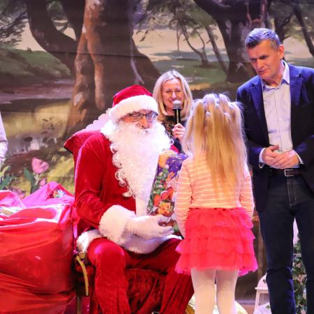 Burmistrz Drzewicy wraz z Mikołajem wręczają prezent występującej dziewczynce