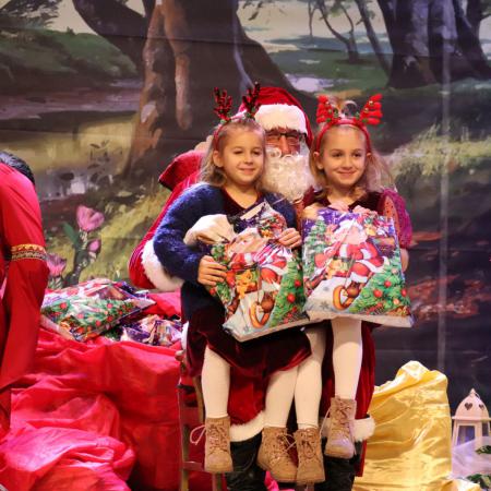 Dwie dziewczynki siedzą u Mikołaja na kolanach podczas wręczania prezentów