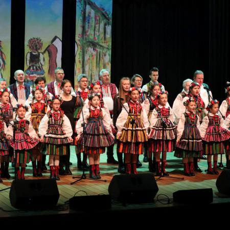 Grupa osób w ludowych strojach śpiewa na scenie podczas koncertu dla Ukrainy