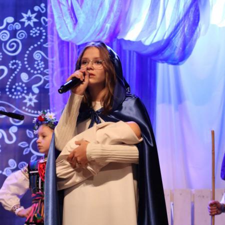 Dziewczyna w stroju Maryi z dzieciątkiem na rękach Śpiewa przy mikrofonie na scenie
