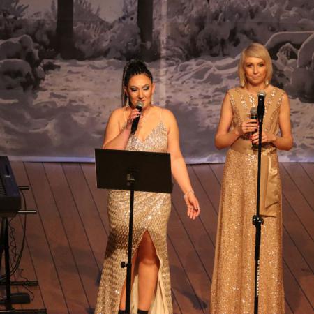 Dwie kobiety w złotych sukniach zapowiadają koncert gwiazd