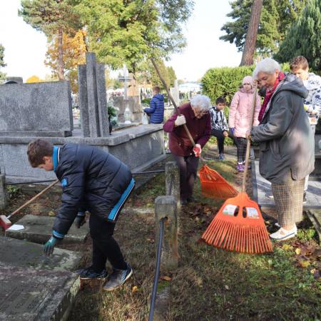 Grupa osób sprząta cmentarz