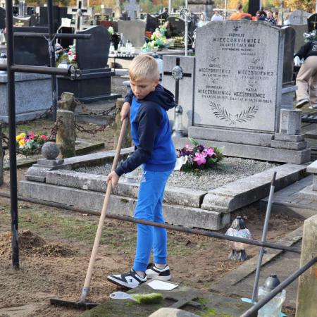Chłopiec sprząta teren przy zabytkowym grobie
