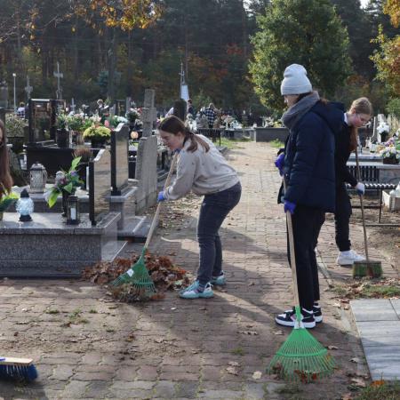 Młodzież grabi alejkę przy grobach na cmentarzu