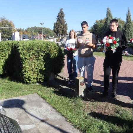 Młodzież składa wiązanki i znicze na grobach.