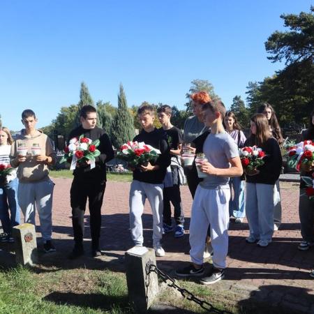 Uczniowie SP w Drzewicy wraz z dyrektor RCK składają wiązanki i znicze.