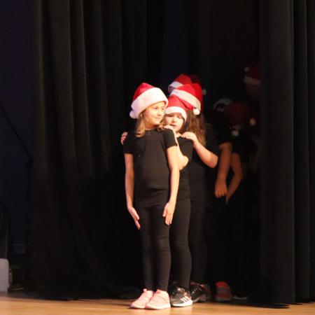 Dziewczynki w czapkach Mikołaja stoją w rzędzie ma scenie  