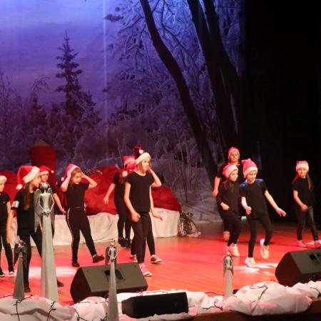 Dzieci ubrane na czarno w czapkach Mikołaja tańczą na scenie 