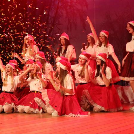 Dziewczyny ubrane w czerwone spódnice siedzą na scenie  