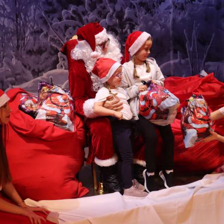 Mikołaj trzyma na kolanach dzieci z paczkami