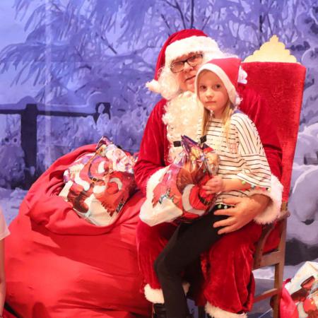 Mikołaj trzyma na kolanach dziewczynkę z paczką 