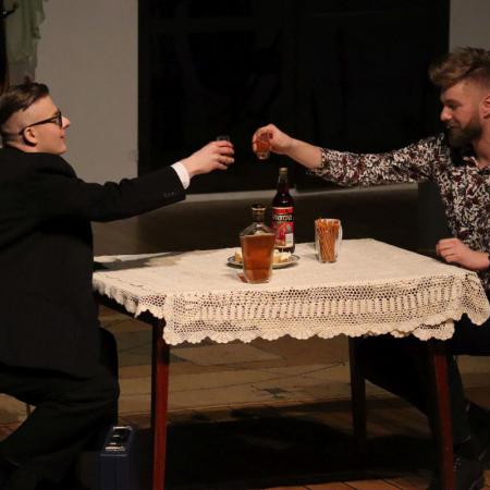Dwaj mężczyźni siedzą przy stole ,wznoszą toast.
