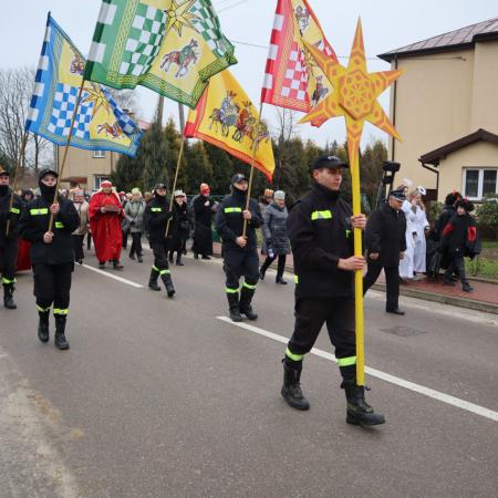 Strażacy niosący flagi Trzech Króli i gwiazdę idąc po ulicy 
