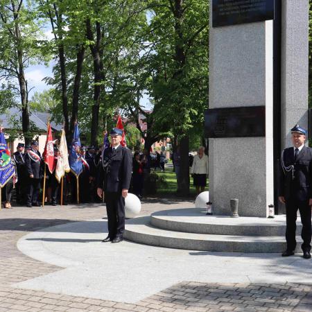 Strażacy stoją na baczność pod pomnikiem 