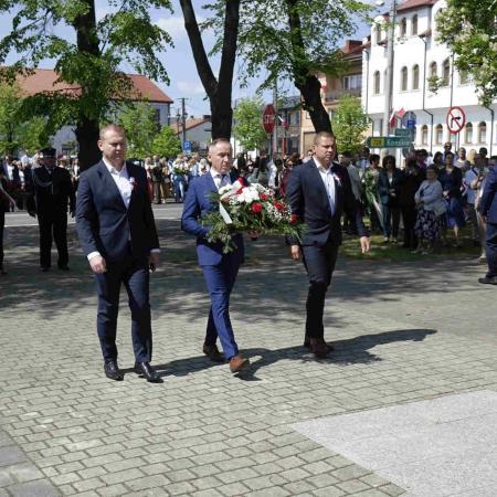 Trzech mężczyzn niesie wieniec pod pomnik 