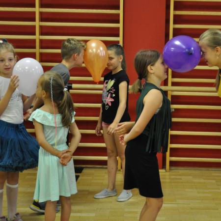 Kilka par dzieci stoi naprzeciw siebie podtrzymując głowami balony
