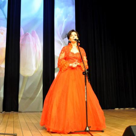 Kobieta w czerwonej sukni śpiewa przy mikrofonie na scenie