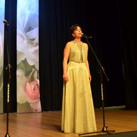 Kobieta w złotej sukni spiewa na scenie przy mikrofonie