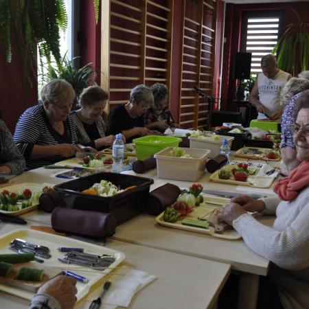 Kobiety siedzące przy stole wykonują ozdoby z warzyw i owoców