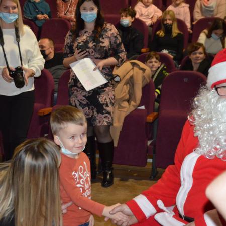 Mikołaj wręcza preznety dzieciom, w tle osoby które przyszły oglądać bajkę